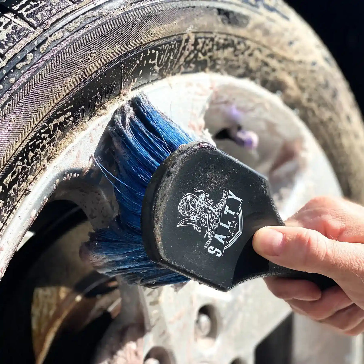 Person cleaning a tire with a blue brush labeled 'Salty'.