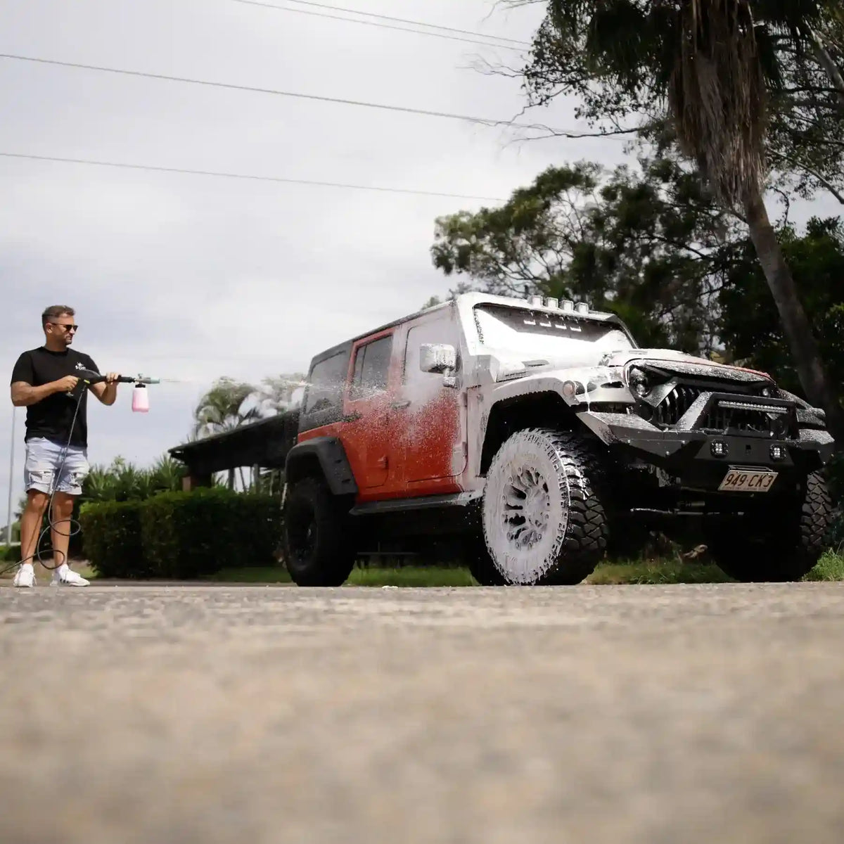 Person washing a red and black off-road vehicle with a hose on a driveway.