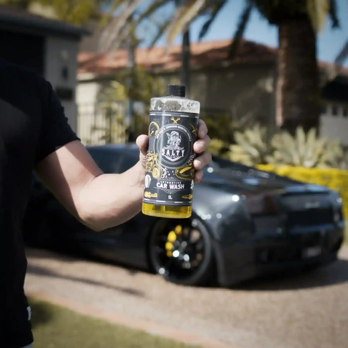 Person holding a bottle of car wash soap with a car in the background