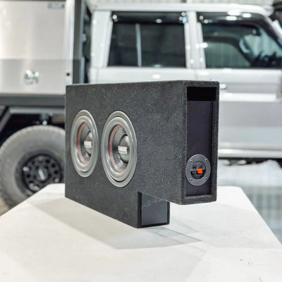 Car subwoofer box on a car's open trunk with a white SUV in the background