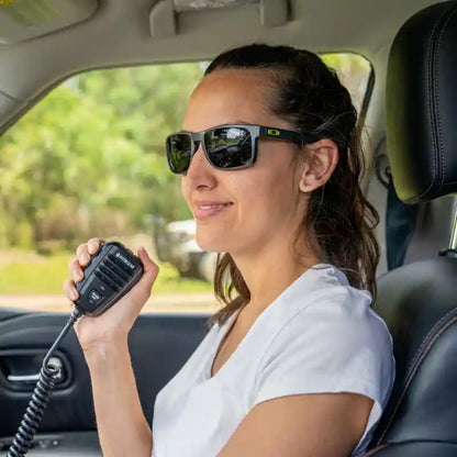 Woman in a car holding a radio communication device, wearing sunglasses.