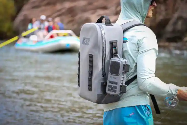 Person with a backpack and radio near a river with rafts in the background