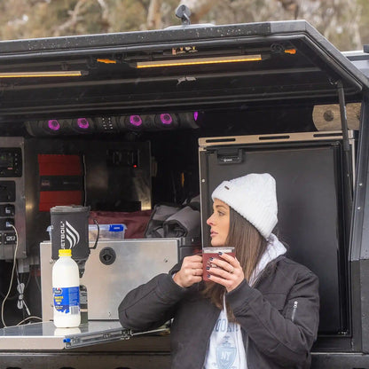 Person drinking from a cup inside a vehicle with equipment and supplies visible