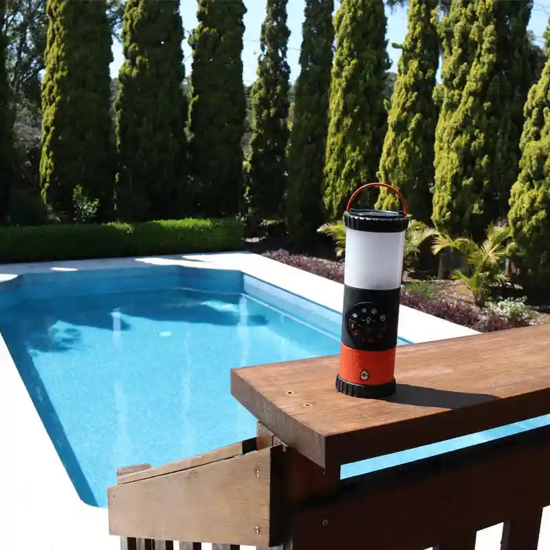 Portable lantern on a wooden deck by a pool with trees in the background