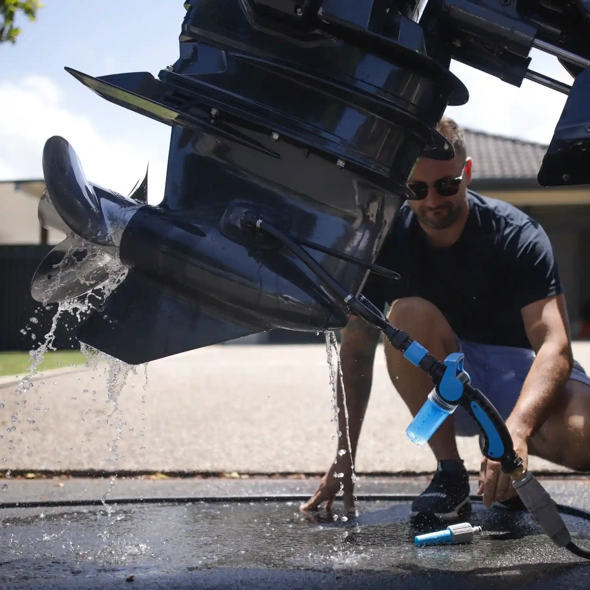 Person cleaning a boat propeller with a hose outdoors.