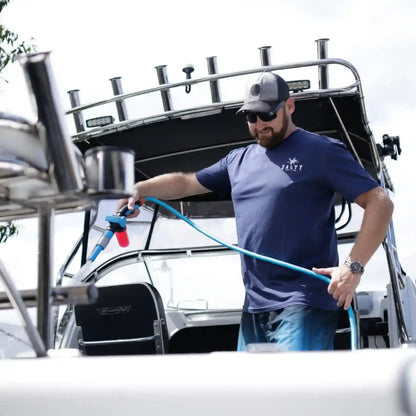 Man cleaning a boat with a pressure washer, wearing a blue shirt and cap.