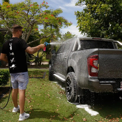 Person washing a black pickup truck with a garden hose outdoors.