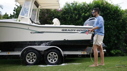 Man washing a Grady-White boat with a hose on a grassy area.