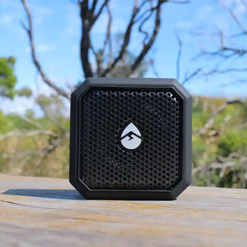 Black portable speaker with a brand logo on a wooden surface with a natural background