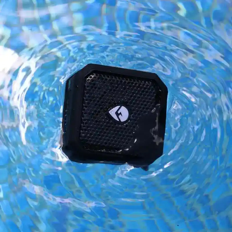 Black portable speaker floating on water with a visible brand logo.
