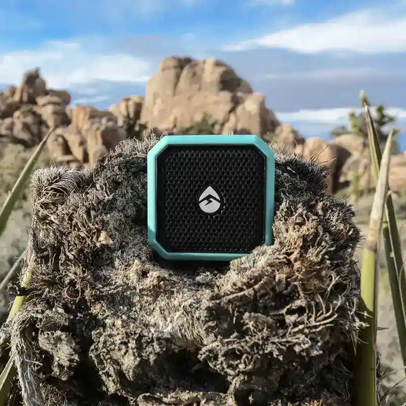 Teal and black portable speaker on a rocky surface with desert landscape in the background
