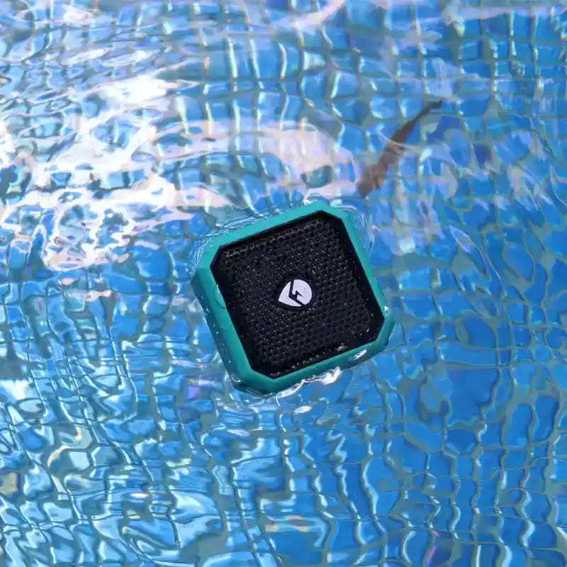 Teal Bluetooth speaker floating on water with a clear blue background