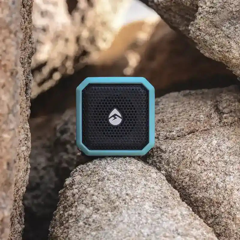 Portable speaker with a brand logo on a rocky surface
