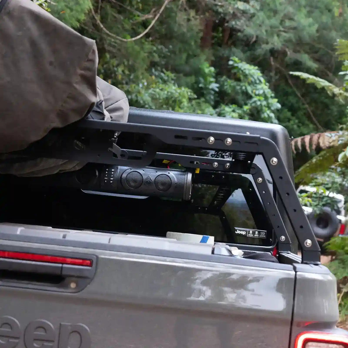 Back of a Jeep with an open tailgate and roof rack in a forest setting