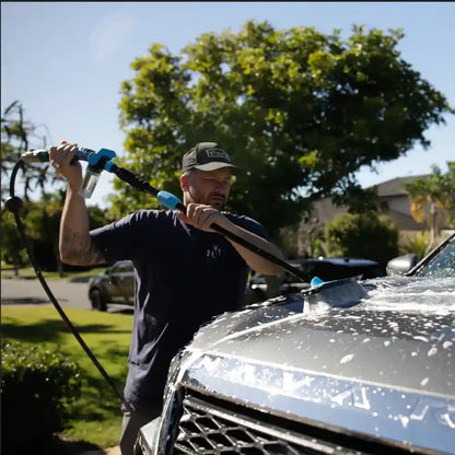 Man washing a car with a pressure washer in a suburban setting