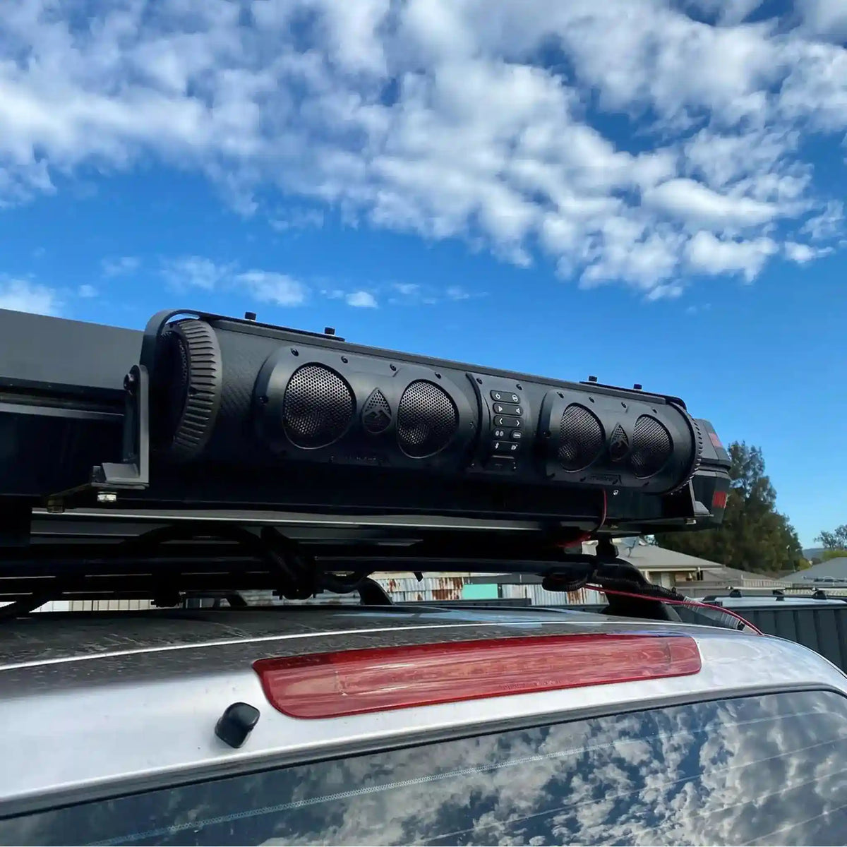 Roof rack with a large black speaker system against a blue sky.