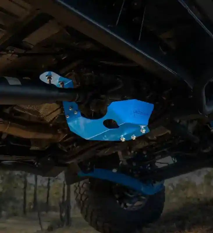 Blue transfer case protector on a LandCruiser 70 Series vehicle, with a blurred natural background.
