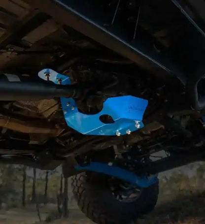 Blue transfer case protector on a LandCruiser 70 Series vehicle, with a blurred natural background.