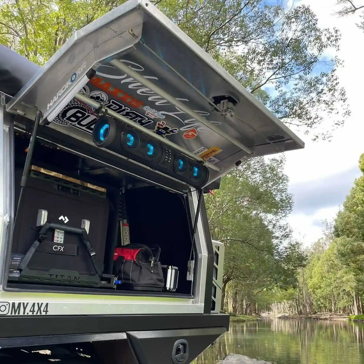 Truck bed with storage compartments open, showing equipment, against a natural background.